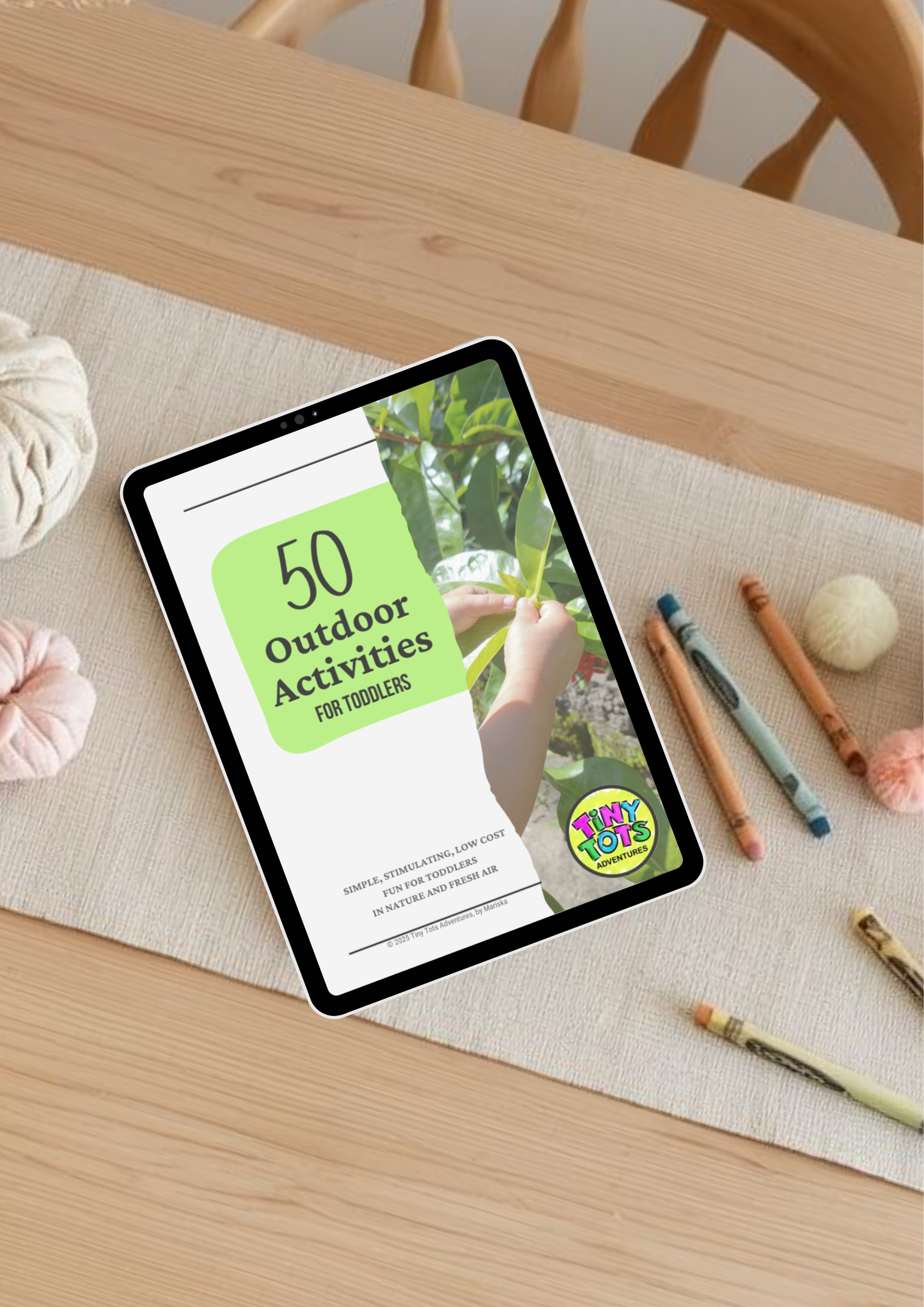 Tablet displaying a children's activity book on a wooden table with craft materials.