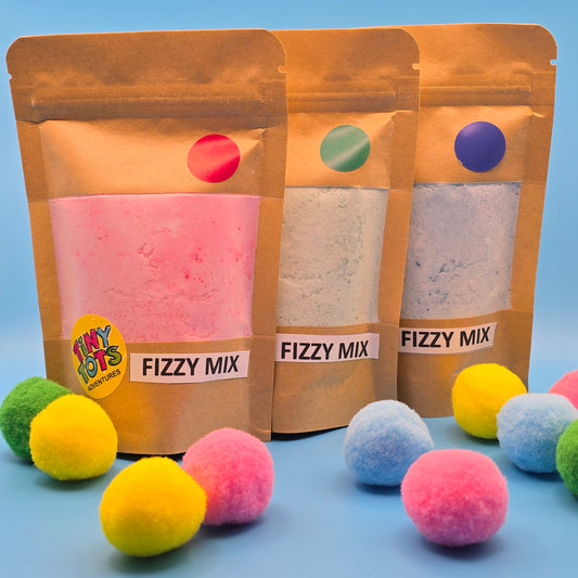 Three packages of Fizzy Mix with colorful pom-poms on a blue background