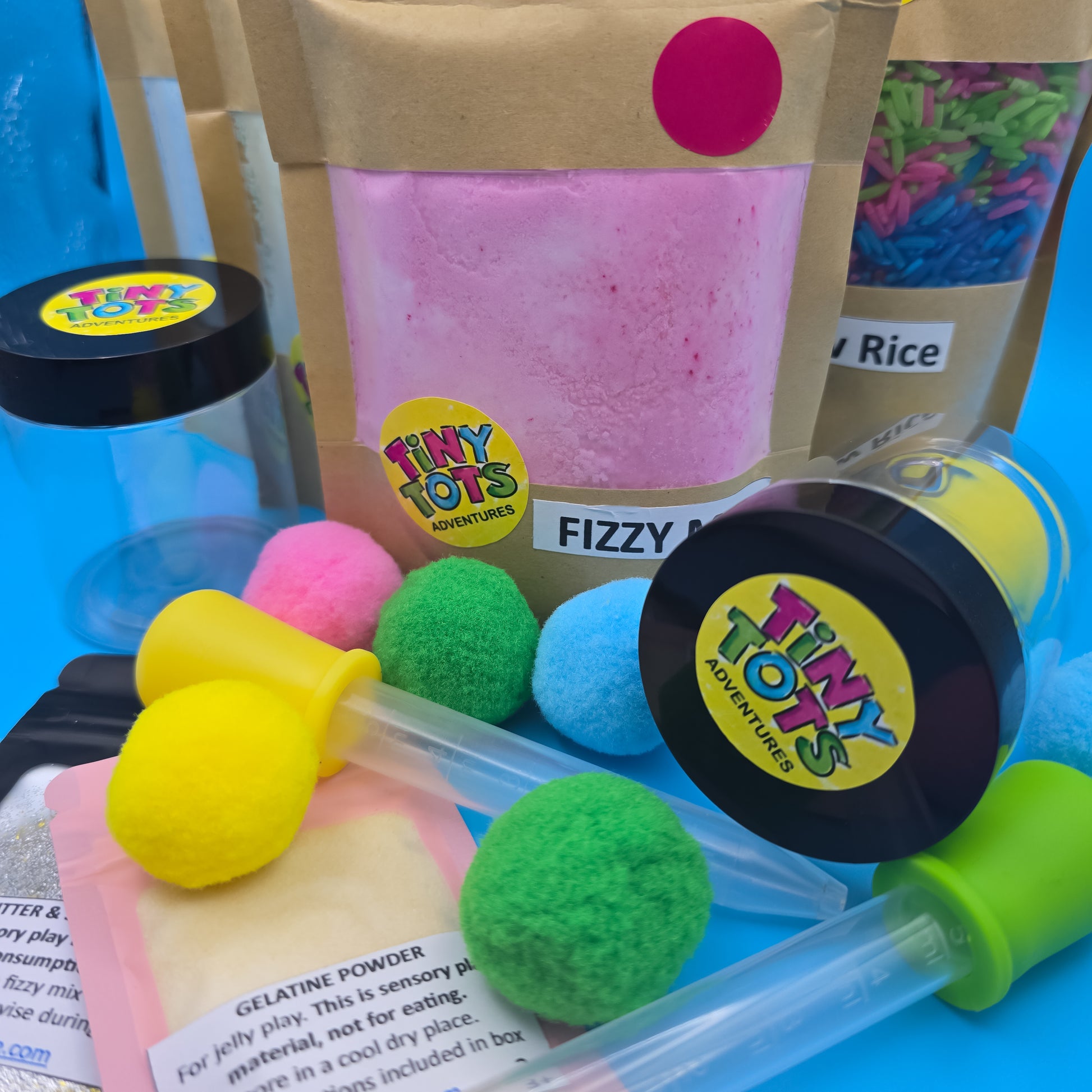Contents of Potions and Play Pack, fizzy mix, rainbow rice, droppers Colorful fluffy balls with a 'Tiny Tots' container on a blue background