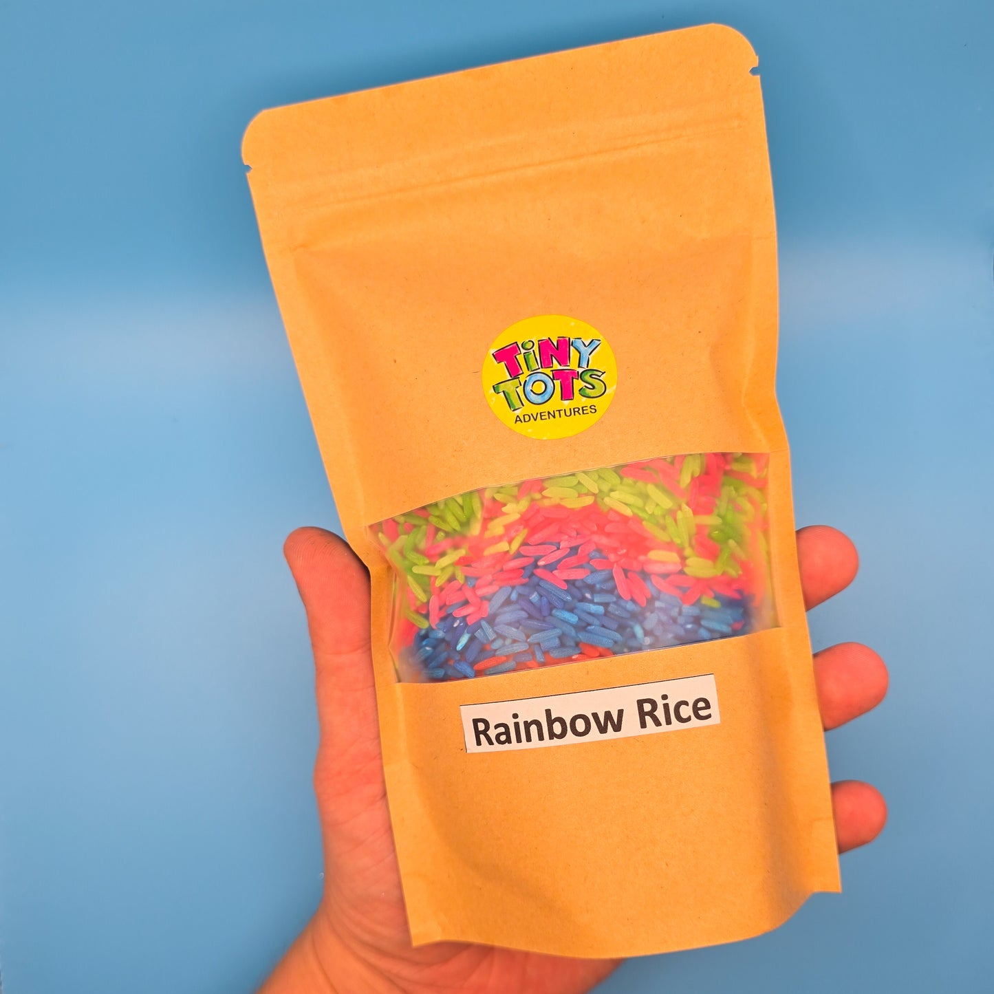paper package of 'Rainbow Rice' with 'Tiny Tots' branding on a blue background