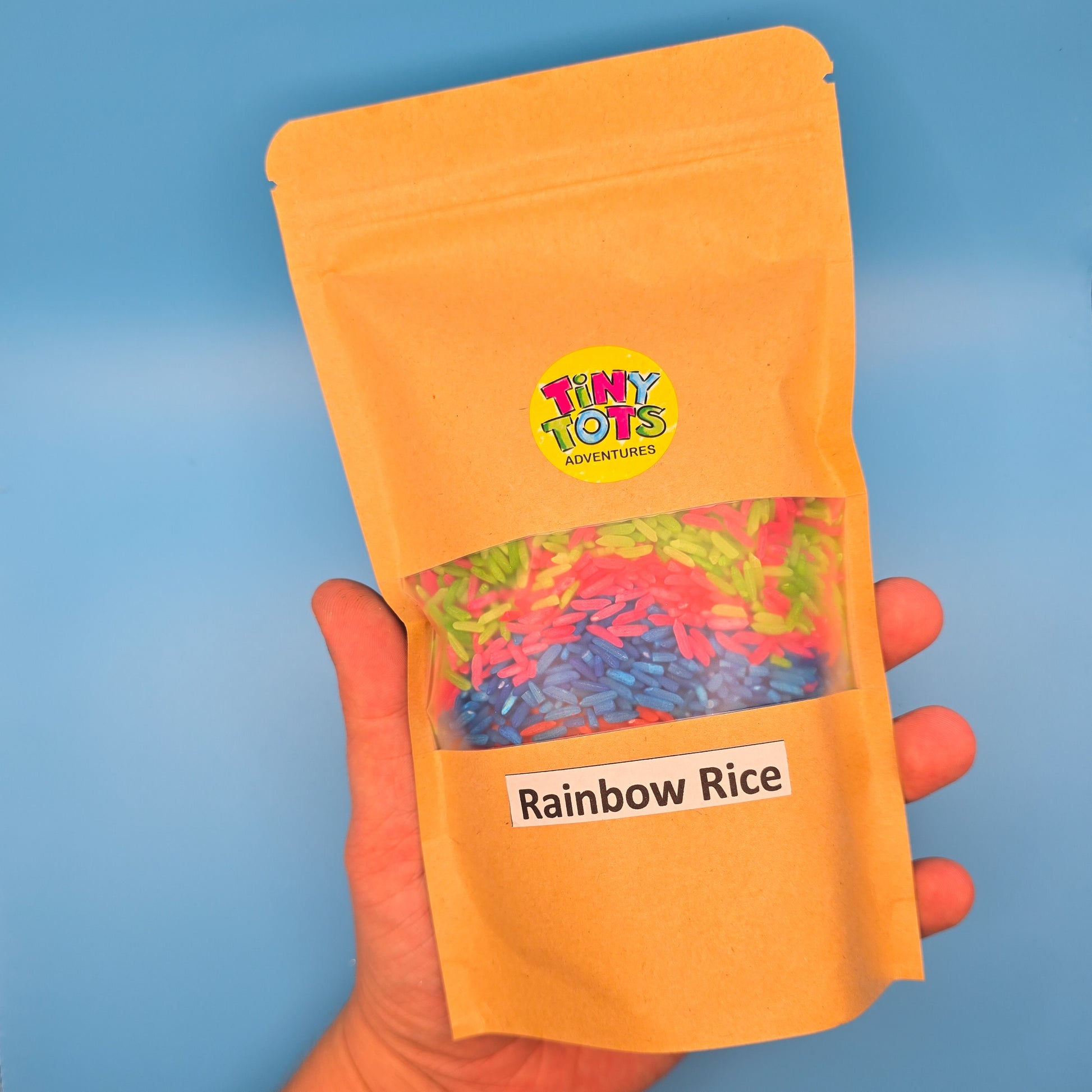 paper package of 'Rainbow Rice' with 'Tiny Tots' branding on a blue background