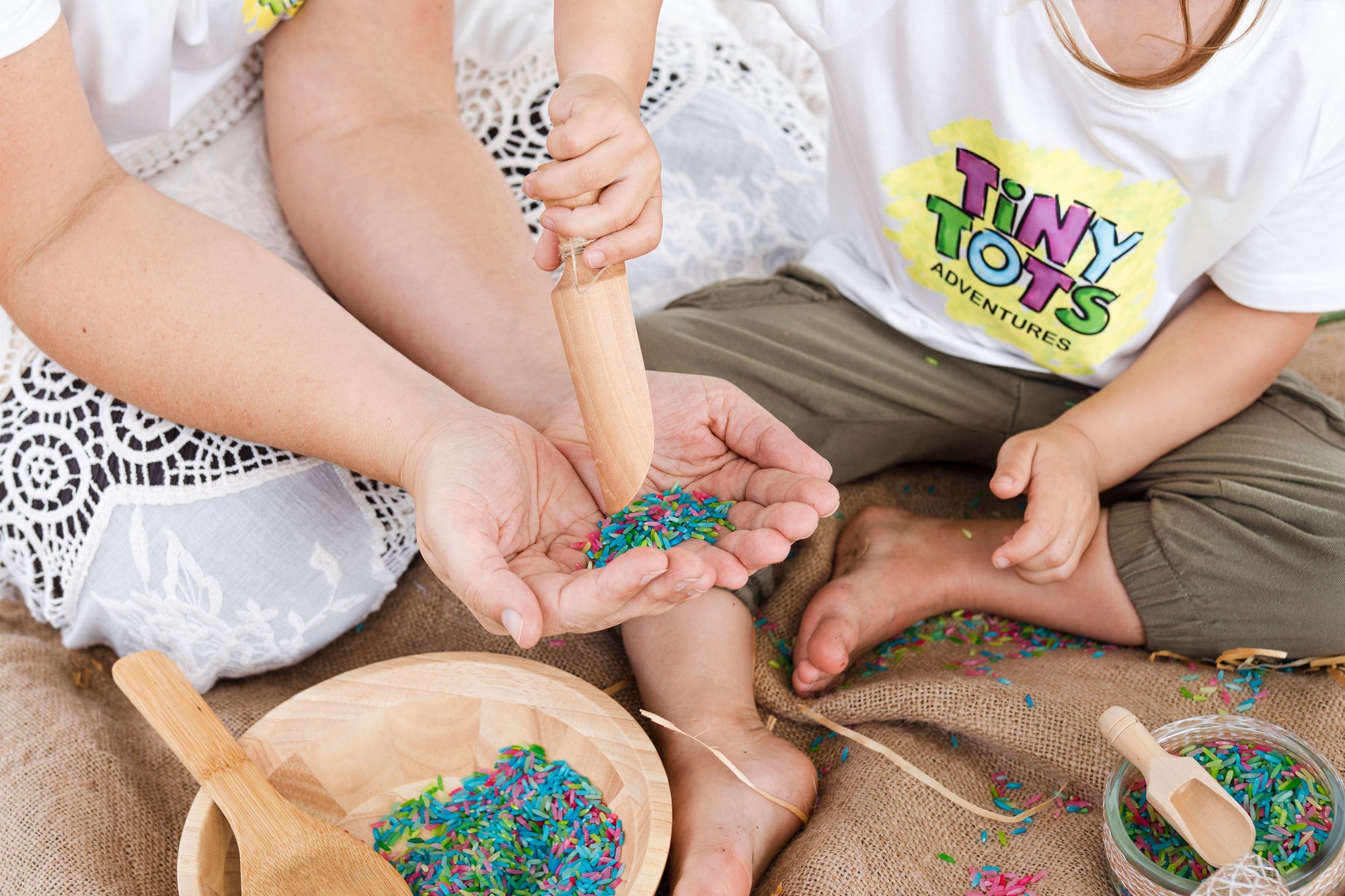 Children playing with colorful materials in a setting with 'Tiny Tots Adventures' branding. rainbow rice sensory play